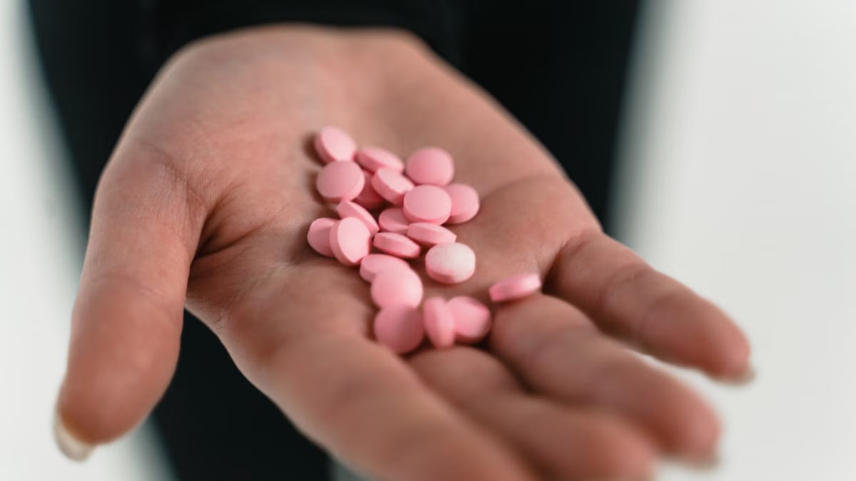 A close-up of a hand holding pink pills, highlighting healthcare concepts.