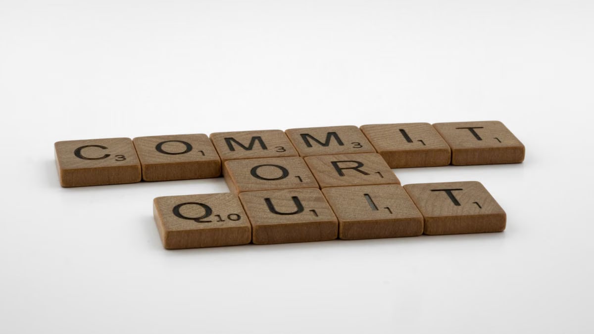 Scrabble tiles spelling 'Commit Or Quit' on a white surface, symbolizing decision-making.